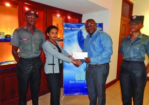 Station Officer Andrew Holder receiving the cheque from a GBTI Marketing Assistant, Tricia Persaud, in the presence of other officers from the Guyana Fire Service
