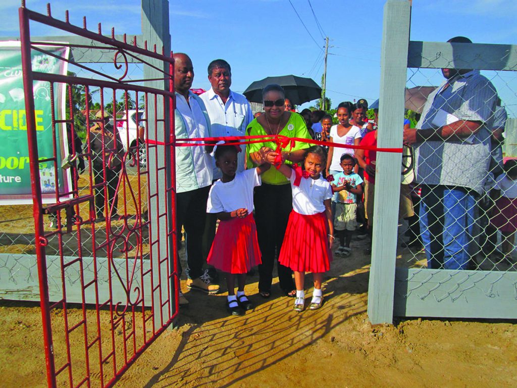 Minister Volda Lawrence assisted by two children cuts the ribbon to open the Play Park