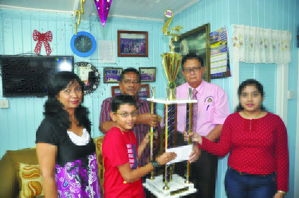 Chairman of the KMTC Cecil Kennard (2nd from right) receives the trophy and cheque from Rohan Booj-Raj (2nd from left) in the presence of Zulika Booj-Raj (center) and children of the late Rovin, Sherisa Booj-Raj (right) and Avanindra Booj-Raj