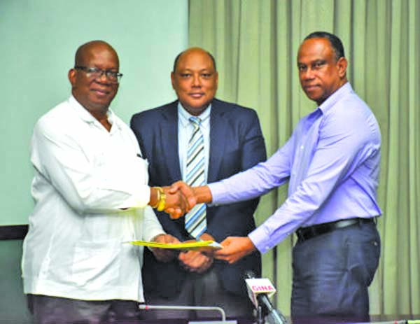 Finance Minister Winston Jordan and GGDMA President  Terrence Adams shake hands after signing two agreements. Also in photo is Natural Resources Minister Raphael Trotman (centre) 