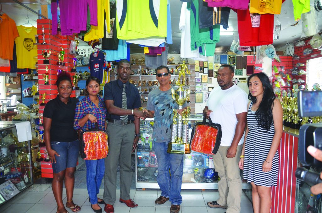 Petra Organisation’s Mark Alleyne collects the trophy from Proprietor Ramesh Sunich while staff members and Troy Mendonca (second from right) look on 