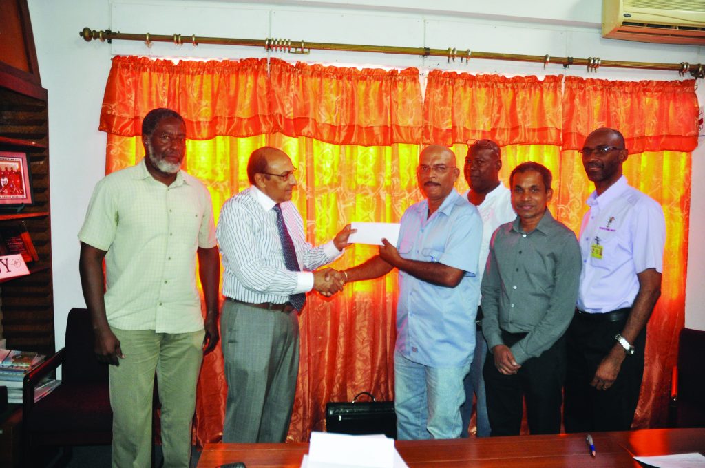 GOA  President K A Juman Yassin gleefully hands over the cheque to Mahendra Persaud in the presence of members of the GOA and GNRA at Olympic House  