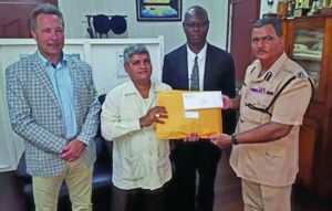 In photo are Minister within the Finance Ministry, Jaipaul Sharma handing over the reports to acting Police Commissioner David Ramnarine, in the presence of ACP Sydney James and British Advisor to SOCU, Dr Sam Sittlington