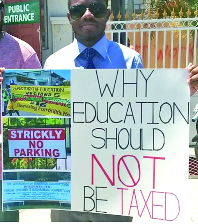 A protester outside GRA holds a placard highlighting several grammatical errors which have appeared on Finance and Education Ministries’ properties, as well as on a banner during the recent Children’s Mashramani 